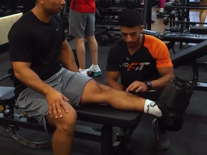 Instrutor da Led Fit ajustando um exercício com um aluno no banco de treino